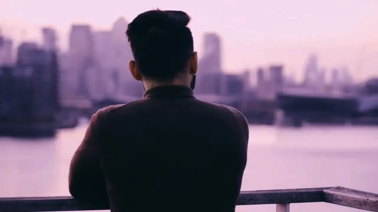 Homem de costas observando o horizonte de uma cidade às margens de um rio